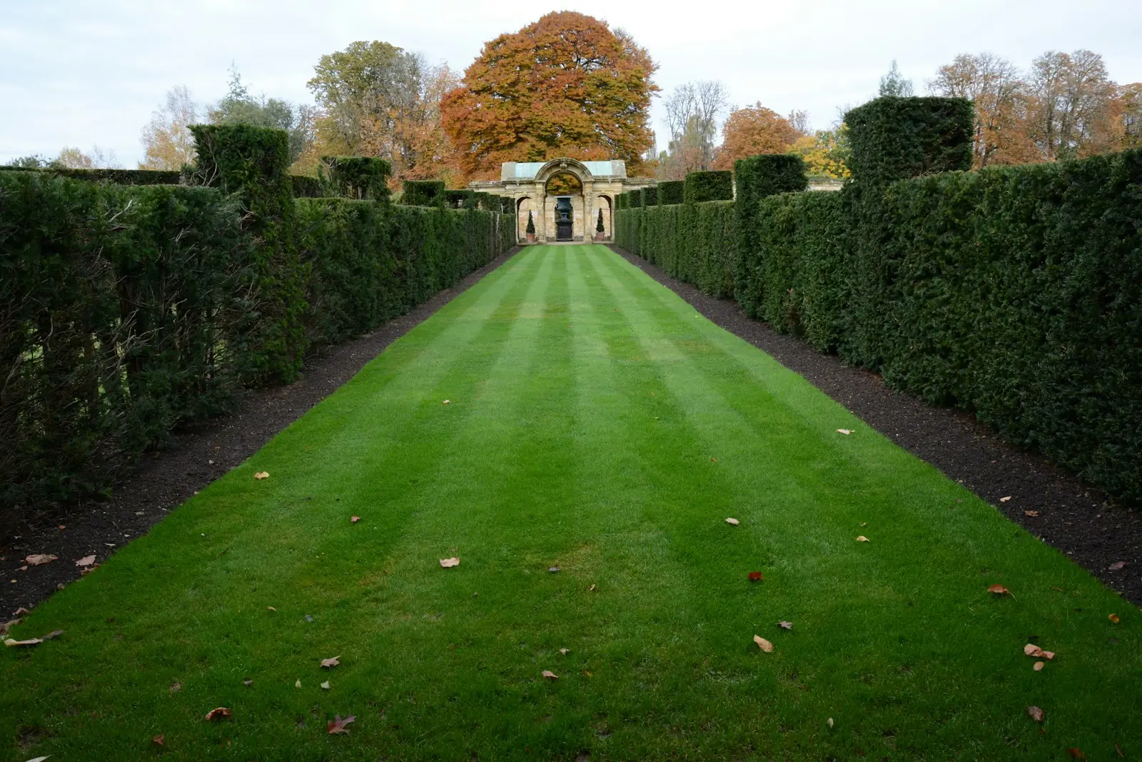 Long striped lawn framed by tall clipped hedges leading to a stone garden building